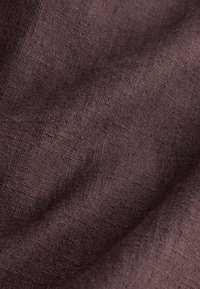 Ciemnobrązowa tkanina o teksturze z widocznymi, plecionymi włóknami i miękkimi fałdami tworzącymi delikatne cienie.