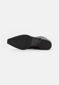 Suela de zapato de cuero negro con punta afilada, banda de rodadura de goma negra texturizada y un tacón ligeramente elevado para mayor estabilidad.