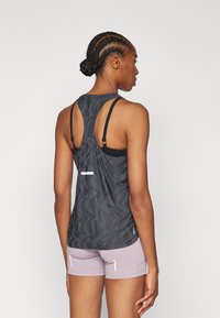 Top atletico nero a motivi con design racerback, caratterizzato da un accento riflettente bianco e abbinato a pantaloni corti viola chiaro.
