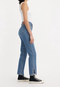 Vaqueros de tiro alto azul claro con corte recto, con aberturas laterales en el bajo, hechos de tela vaquera. Combinados con zapatillas negras de caña alta.