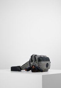 Sac rayé noir et blanc avec deux compartiments à fermeture éclair, une sangle réglable et une petite peluche de singe attachée à l'avant.