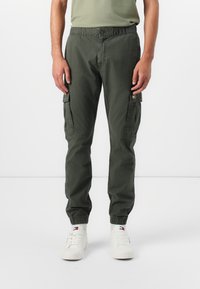 Khaki Cargo-Hosen mit elastischem Bund und Bündchen, ausgestattet mit Seitentaschen und einem weichen, atmungsaktiven Stoff. Getragen mit weißen Sneakers.