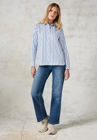 Button-up shirt in light blue with navy vertical stripes, paired with flared blue jeans and light-colored sneakers. Casual outfit.