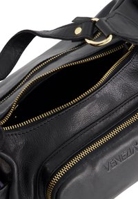 Black leather handbag with gold zippers, one open showing interior, and embossed "VENEZIA" logo on the front pocket.