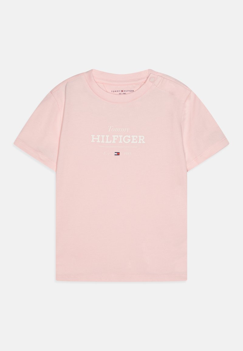 Rožinė medvilninė marškinė su trumpomis rankovėmis, apvaliu kaklu ir balta išspausdinta tekstu "Tommy HILFIGER" su logotipu žemiau. Užsegimas ant peties.