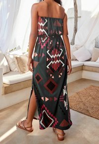 Abito maxi senza spalline con motivo geometrico in bordeaux, bianco e rosa su uno sfondo scuro. Fessura laterale e dettaglio in vita elasticizzata.