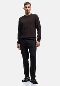 Donkerbruine geribbelde langetermijntrui gecombineerd met zwarte broek en zwarte schoenen. De outfit heeft een gestructureerde stof en een relaxte pasvorm.