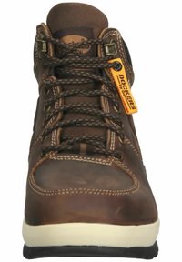 Botte montante en cuir marron avec lacets noirs et marron, semelle blanche, coutures visibles et étiquette orange Dockers by Gerli sur le côté.