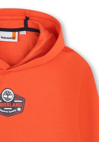 Oranje hoodie van zachte stof, met een rond logo-opdruk van een boomontwerp en de tekst "Timberland" in zwart en wit. Met capuchon.