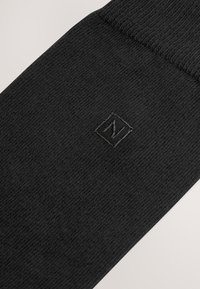 Black sock with ribbed texture, featuring a subtle embossed logo in a square at the center. Material appears soft and knitted.