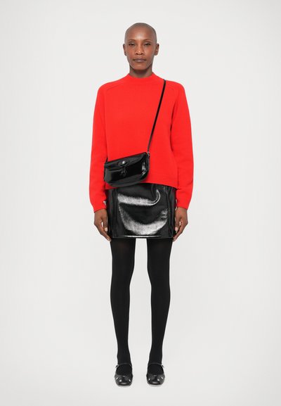 Red knitted sweater, black glossy mini skirt, black tights, and black studded shoes; small black crossbody bag with a curved design.