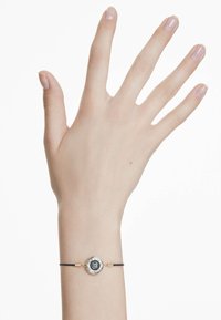 Svart snörarmband med en rund metallpussel som har en central blå och svart design, gyllene accenter och en slät, polerad yta.