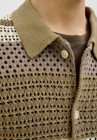 Polo shirt in maglia all'uncinetto in toni terrosi di beige e marrone, caratterizzato da un motivo testurizzato, placca dei bottoni e design del colletto.