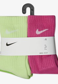 Sześć par skarpetek załogowych w kolorze zielonym i różowym, wykonanych z prążkowanej tkaniny, z białymi logo Nike w kształcie łuku oraz etykietą z tektury.