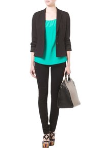 Schwarzes Blazer, türkisfarbenes Tanktop, schwarze Skinny-Hose und Plateausandalen. Trägt eine zweifarbige Handtasche mit schwarzem Grund und grauen Akzenten.