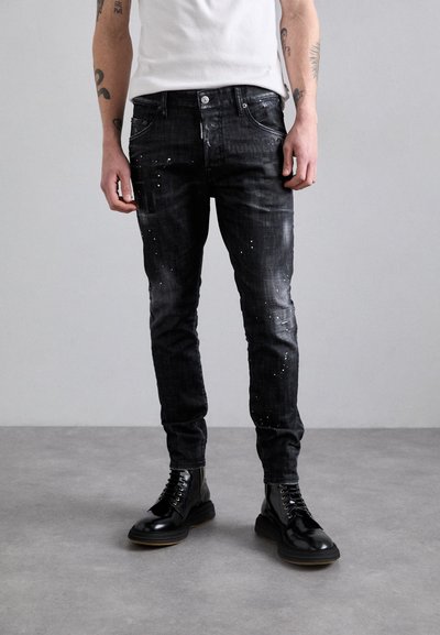 Jeans neri con vestibilità slim, texture rovinata e dettagli con spruzzi di vernice bianca. Indossati con stivali neri stringati.