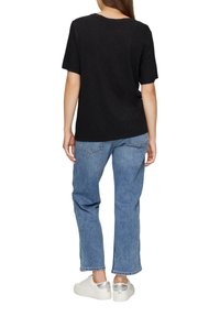 Schwarzes T-Shirt mit kurzen Ärmeln, kombiniert mit hellblauen geraden Jeans und weißen Sneakern mit einem silbernen Akzent an der Ferse.