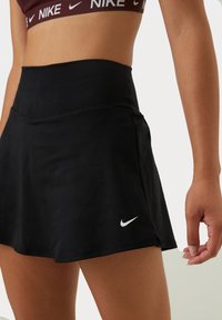Falda atlética negra con una cintura alta, textura suave y logo de Nike en blanco, con un diseño acampanado para facilitar el movimiento.