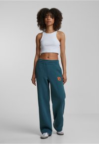 Joggers verde azulado con un logo naranja bordado; de talle alto, corte relajado; combinados con una camiseta corta blanca; tela de mezcla de algodón suave.