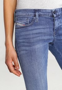 Jeans de denim azul claro con un diseño clásico de cinco bolsillos, un ligero desvanecimiento y detalles de costura decorativa en el bolsillo frontal.