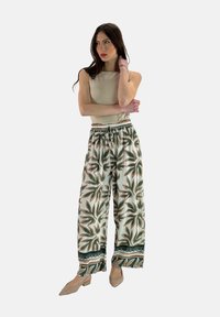 Brede, gestreepte broek met een groen en bruin bladdesign op een lichte achtergrond; elastische tailleband, gecombineerd met een aansluitend beige top.