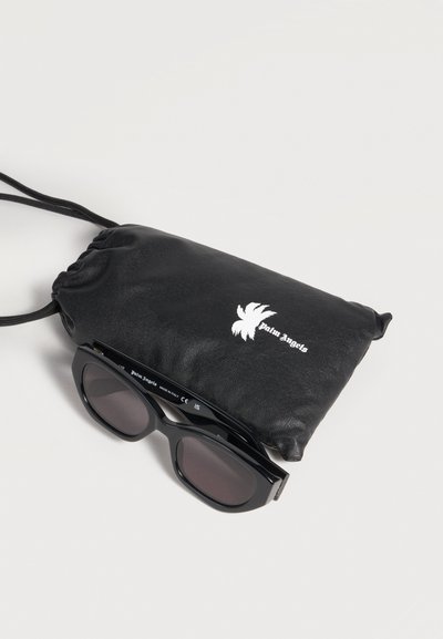 Lunettes de soleil rectangulaires noires avec des verres foncés reposant sur une pochette noire à cordon ornée d’un logo de palmier blanc.