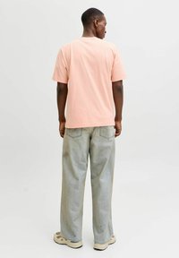 Hele roosa puuvillane T-särk ümmarguse kaelusega ja lühikeste varrukatega, koos laihäärtse hallide teksade ja beežide tossudega.