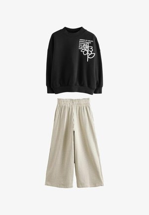Schwarzer Sweatshirt mit weißem Text und floralen Design, kombiniert mit cremefarben gestreiften weitem Hosen, die einen elastischen Bund haben.