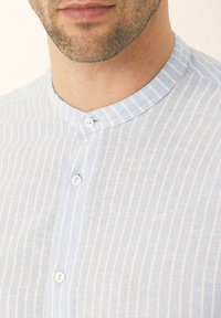 Camicia a righe blu chiaro con colletto alla francese, realizzata in un tessuto testurizzato. Presenta due bottoni al collo e un sottile motivo verticale.