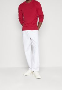 Suéter de punto rojo con cuello redondo y puños acanalados, combinado con pantalones anchos blancos. Zapatillas blancas completan el conjunto.