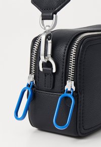 Geantă din piele texturată neagră, cu fermoar argintiu și accente hardware albastre. Prezintă o formă rectangulară și o curea detașabilă.