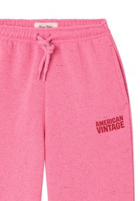 Pink sweatpants with elastic waistband and drawstring, featuring "AMERICAN VINTAGE" text in red on the upper thigh area.