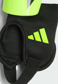 Guante de neopreno negro con un logo verde de Adidas, tejido texturizado, correa ajustable y un acento amarillo neón cerca de un artículo de color similar.