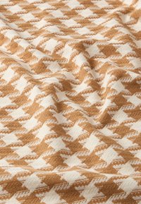 Tissu à motif pied-de-poule brun et crème, texturé avec une finition douce et tissée, drapé pour montrer la profondeur et les détails du design.