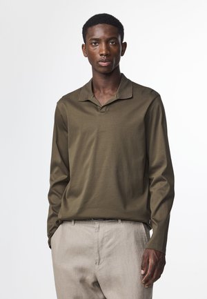 Olijfgroene polo met lange mouwen, gemaakt van een zachte stof en met een open kraag, gecombineerd met lichte beige broeken.