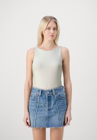 Lys grønn ermeløs bodysuit kombinert med en denim mini-skjørt med frynset kant. Outfitten har en tettsittende design og en avslappet stil.
