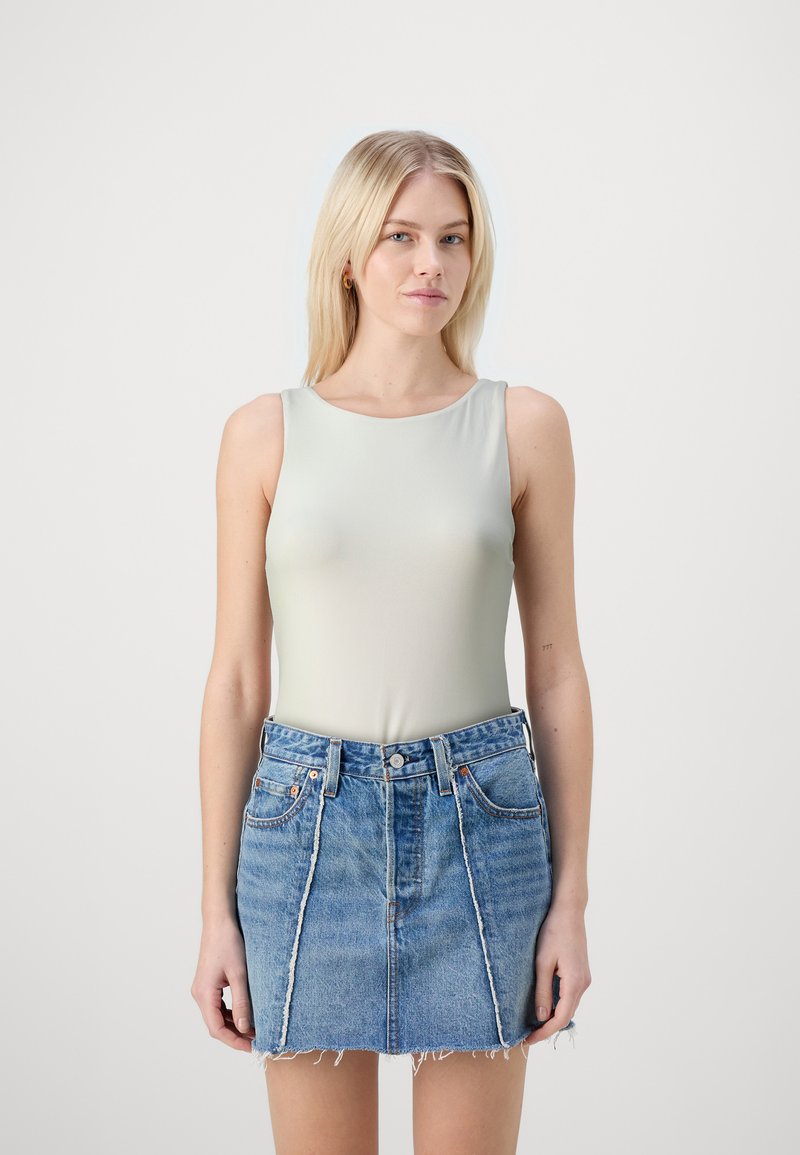 Lys grønn ermeløs bodysuit kombinert med en denim mini-skjørt med frynset kant. Outfitten har en tettsittende design og en avslappet stil.