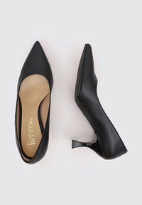 Zapatos de tacón alto de cuero negro con punta puntiaguda y un tacón bajo y transparente. Textura lisa con una plantilla beige que presenta una marca en dorado.