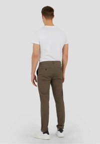 Pantalon kaki avec une coupe slim et des jambes fuselées, doté de deux poches arrière. Porté avec un t-shirt blanc et des baskets blanc-noir.