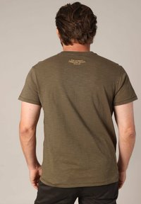 T-shirt olive, à manches courtes, en tissu texturé, avec un petit logo doré dans le haut du dos. Design classique à col rond.