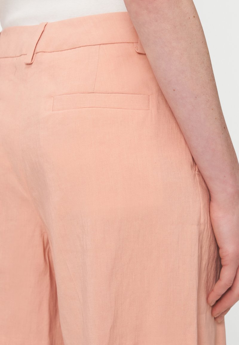 Helle rosa Leinenhose mit glatter Textur, ausgestattet mit einer Gesäßtasche und einem taillierten Design. Von der Seite gesehen.