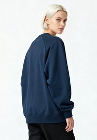 Sweat-shirt bleu marine avec encolure ronde, coupe oversize et poignets côtelés. Texture douce et design minimaliste, porté avec un pantalon noir.