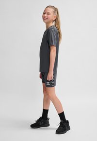 Grijze sportshirt met korte mouwen, gecombineerd met bijpassende shorts met chevronaccenten aan de zijkant en logo, gedragen met zwarte sneakers.