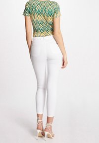 Vita smala jeans med hög midja och bakfickor, i kombination med en mönstrad kortärmad topp i flera färger och strappy högklackade skor.