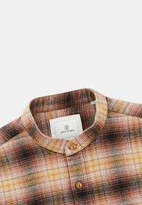 Chemise à boutons en motif tartan avec des nuances de marron, orange et beige ; dotée d'un col rond et d'une étiquette cousue à l'intérieur.