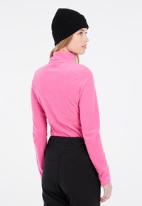 Golf in pile fucsia, maniche lunghe, texture morbida. Abbinato a pantaloni neri con design elegante e accenti sottili.