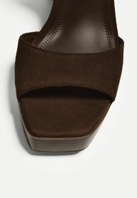 Sandal platform in suede marrone con ampia fascia incrociata, fodera interna liscia e tacco in legno impilato. Presenta dettagli di cucitura sulla fascia.