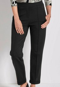 Zwarte broek van gladde stof, met een getailleerde pasvorm, voorplooien en opgerolde manchetten. De tailleband is hoog voor extra comfort.