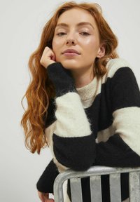 Maglione a righe in nero e crema, realizzato in tessuto morbido e texturizzato. Presenta un colletto a coste e maniche lunghe.