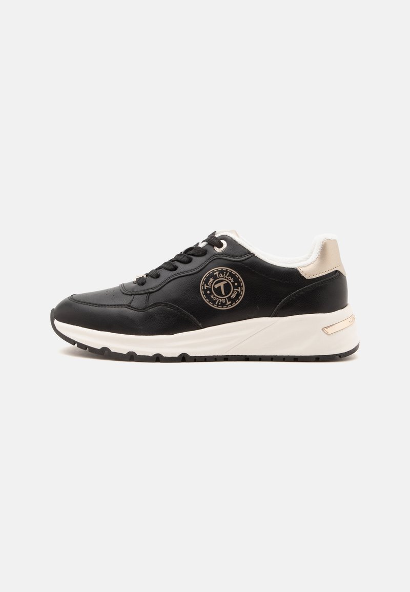 Baskets noires à lacets avec semelle blanche et détail beige au talon, avec un logo circulaire sur le côté sur un fond uni.